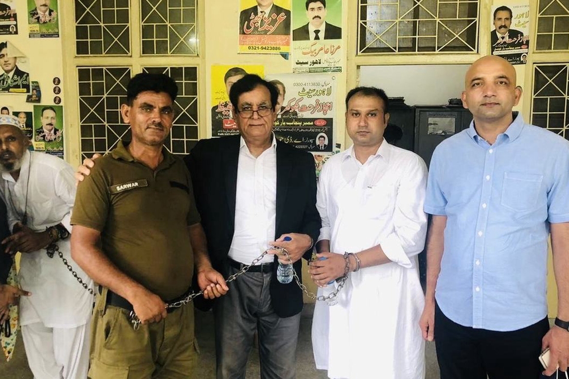 Asif Pervaiz in a white prison uniform alongside a guard, lawyer Saif ul-Malook, and Sajid Christopher from HFO on the far right, during a previous court hearing.