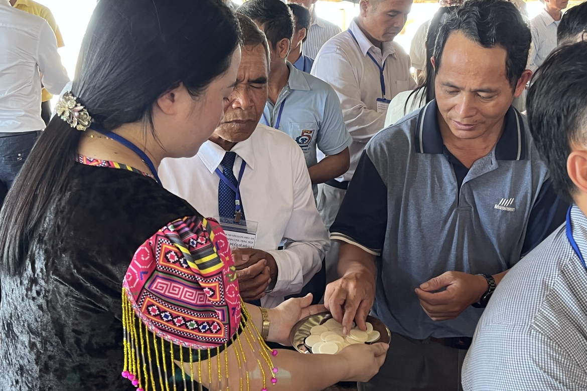 Dien, in traditional Hmong attire, offers communion to male pastors during a conference.