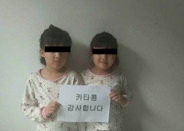 Tvillingene holder skiltet  hvor det på koreansk står: «Katakombene - tusen takk!». «Katakombene» er et navn som brukes om Helpings Hands Korea, partneren til Stefanusalliansen.